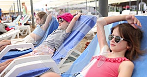 Three happy girls lie on sun loungers and look at sea