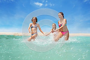 Three happy girls running in the sea splashing