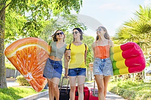 Three happy girls walking with inflatable mattresses at the beach outdoors in summer celebrating vacation. friends having fun on