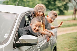 Three happy kids are waving their hands through their car windows