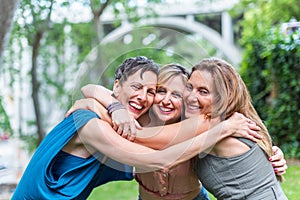 Three happy mature female friends hugging together and looking to camera