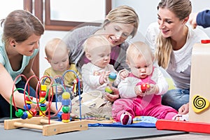 Three happy mothers watching their babies playing with safe toys photo