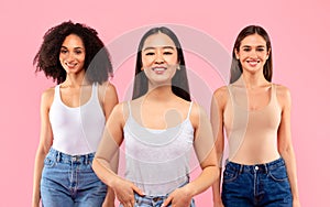 Three happy multiethnic women posing over pink studio background and smiling to camera, studio shot