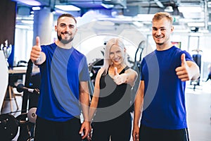 Three happy people at the gym showing thumbs up.