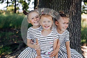 Three happy sisters in dresses smile and hug in the park. Happy childhood. The twins