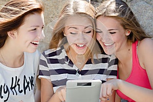 Three happy teen girl friends and tablet computer