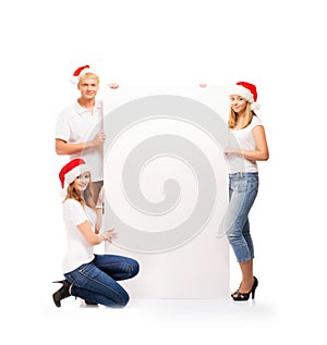 Three happy teenagers in Christmas hats holding a banner