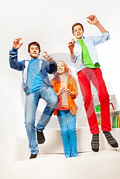 Three happy teenagers jumping on white sofa