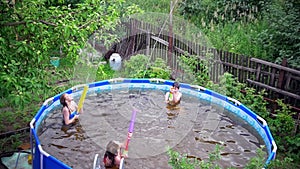 Three happy teenagers shooting with water guns in swimming pool outdoors