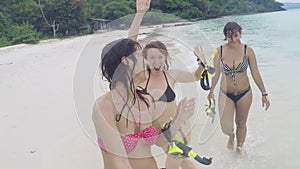 Three happy women wearing bikinis partying at the beach going with snorkeling masks in their hands