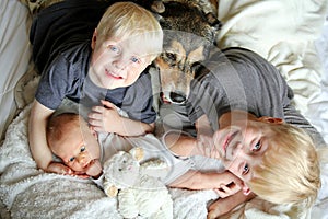 Three Happy Young Children Snuggling with Pet Dog in Bed