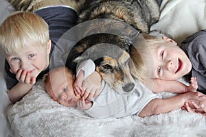 Three Happy Young Children Snuggling with Pet Dog in Bed