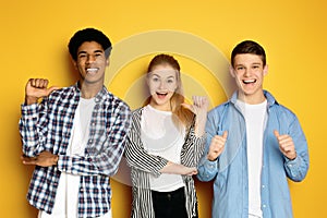 Three Happy Young Friends Gesturing Thumbs-Up Against Bright Yellow Background