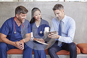 Three healthcare workers sit using tablet computer together