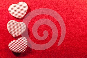 Three hearts made of cloth with red white checkered pattern arranged on a red velvet background with copy space, flat lay,