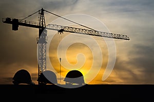Three helmet silhouette at construction site with crane background and sunset