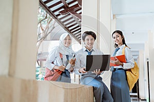 three high school students smiling at the camera while standing on a laptop computer, carrying books, and wearing a bag