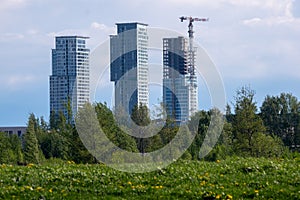 Three highrise buildings standing behing large bushes against cloydy sky