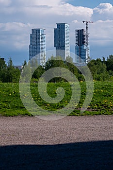 Three highrise buildings standing behing large bushes against cloydy sky