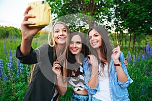 Three hipsters girls blonde and brunette taking self portrait on polaroid camera and smiling outdoor. Girls having fun together