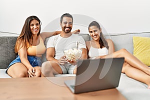 Three hispanic friends watching film using laptop home