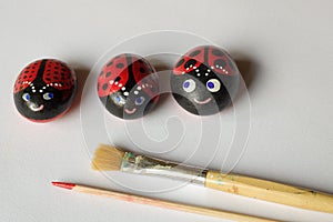 Three home made painted stones as ladybugs on white background,