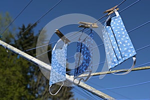 Three  homemade community face masks from cotton cloth after washing drying on a clothesline against a blue sky, protection