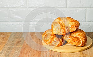 Three homemade croissants are placed on a wooden trey