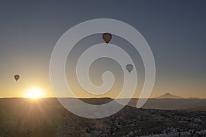 three hot air balloons flying in cappadocia at sunrise, at the Goreme air field at dawn, Erciyes volcano in the background,