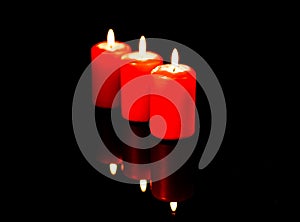 Three hot red candles arranged diagonally are reflected against the background of a black mirror.