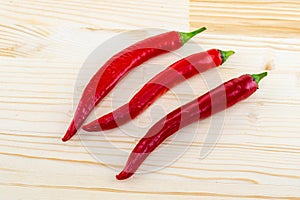 Three hot red chili peppers on a light beige background