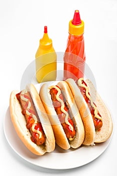 Three hotdogs with mustard and ketchup bottles