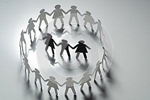 Three human paper figures surrounded by circle of paper people holding hands on white surface. Bulling, segregation photo