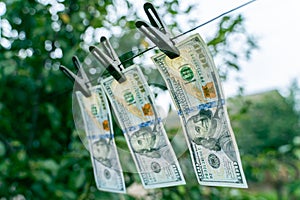 Three hundred dollar bills hanging on a clothes dryer pinned with clothespins close-up on a blurred background. Money laundering