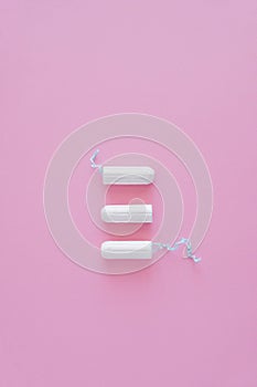 Three hygienic tampons on a pink background.