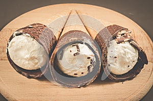 three ice cream with cone in chocolate/three ice cream with cone in chocolate on a round wooden support, selective focus