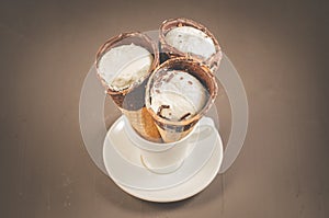three ice cream with cone in chocolate on a in a white cup/three ice cream with cone in chocolate on a in a white cup, top view
