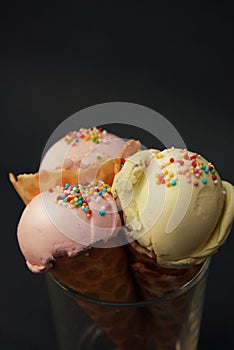 Three ice cream in waffle cone with scoop of pink fruit ice cream and confetti in glass isolated on dark blue background