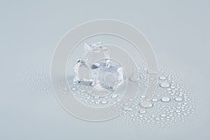 Three ice cubes stacked on a gray background in drops of meltwater.