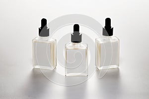 Three identical glass droppers sit side by side on a sleek surface. The droppers feature transparent liquid inside photo