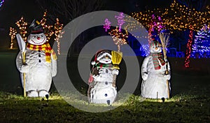 Three Illuminated Snowman Figures With Scarves And Hats Holding Brooms, Displayed At Night