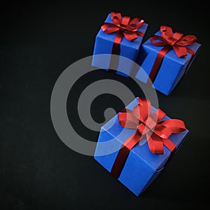 Three indigo gift boxes with red ribbon isolated on black background.