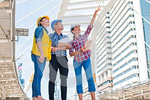 Three industrial engineer standing and looking to right side wear safety helmet with holding inspection and digital tablet