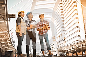 Three industrial engineer standing and looking to right side wear safety helmet with holding inspection and digital tablet