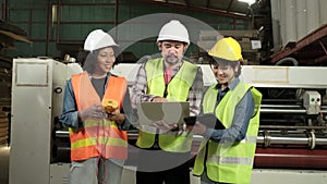 Three industrial workers use a laptop to check a paper manufacturing machine.