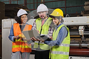 Three industrial workers use a laptop to check a paper manufacturing machine