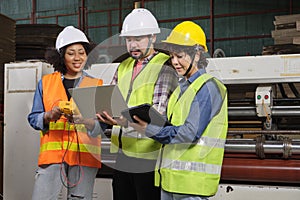 Three industrial workers use a laptop to check a paper manufacturing machine