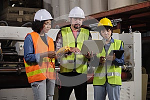 Three industrial workers use a laptop to check a paper manufacturing machine