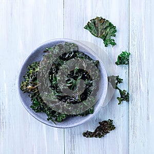 Three ingredient baked green kale chips with sea salt and olive oil, in gray bowl, top view, square format