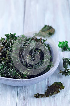 Three ingredient baked green kale chips with sea salt and olive oil, in gray bowl, vertical, copy space